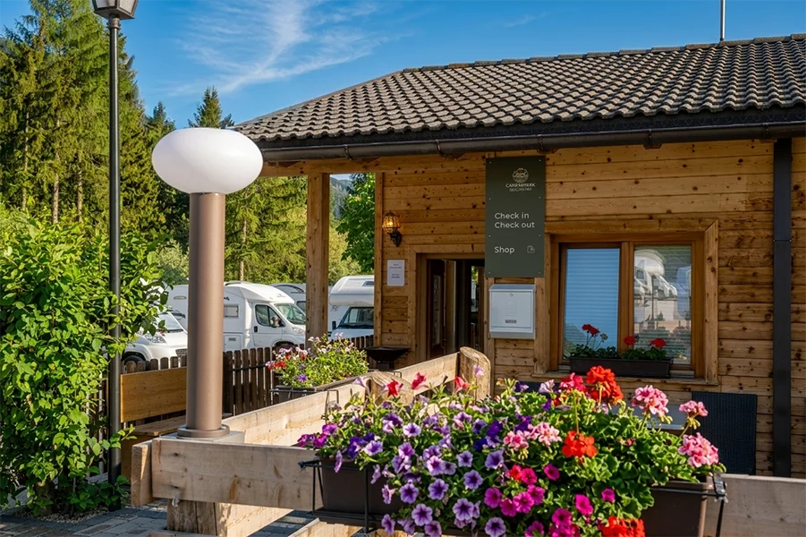 Wooden reception building with check-in and shop sign at a camper van site in the Alps.